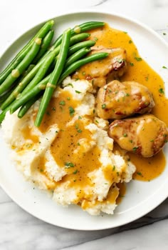 mashed potatoes with gravy and green beans on a white plate next to a fork