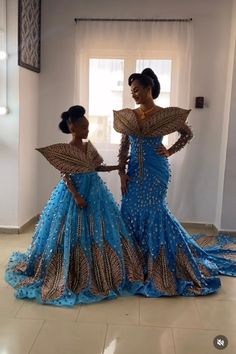 two women in blue and gold dresses standing next to each other on a tile floor