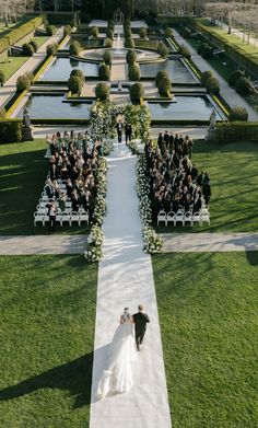 a bride and groom walking down the aisle at their wedding ceremony in front of an elaborate garden