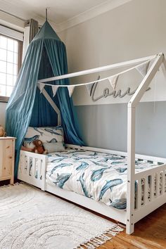 a white bed with blue curtains in a bedroom next to a window and rug on the floor