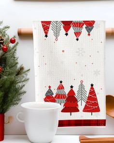 a kitchen towel with christmas trees on it next to a mug and utensils