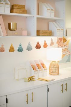 a white desk topped with lots of books and other items next to a lamp on top of a table