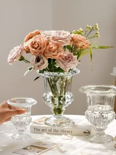 there is a glass vase with flowers in it on top of a table next to two glasses