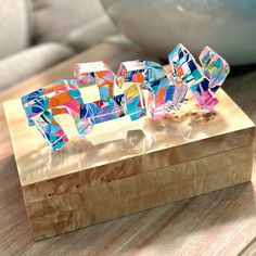 a wooden box with some colorful glass letters on it's sides and a bowl in the background