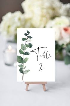 the table numbers were placed on easel with greenery and white flowers in the background