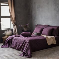 a bed with purple sheets and pillows next to a window