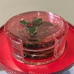 a red plate topped with a glass container filled with liquid and a holly leaf decoration