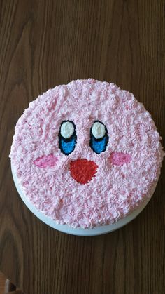 a cake with pink frosting and blue eyes on it's face, sitting on top of a wooden table