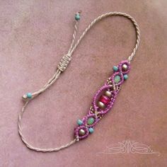 a pink and blue beaded necklace with beads on it's end, sitting on top of a purple surface