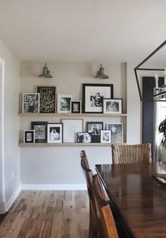 a dining room table with chairs and pictures on the wall above it, along with framed photos