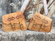 two brown leather bags sitting on top of a cement wall next to each other with buckles