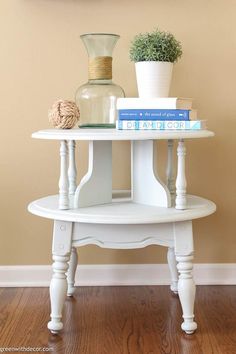 a white table with books and vases on it in front of a tan wall