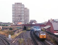 a train is coming down the tracks in front of some buildings and tall buildings on either side