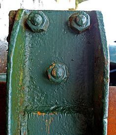 an old green fire hydrant with rivets on it's side and rusted paint