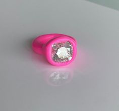 a pink ring with a diamond on it sitting on a white surface, against a gray background