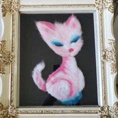 a painting of a pink cat with blue eyes in a gold frame on a wall