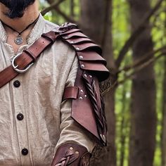 a man dressed in medieval garb standing in the woods with his hands on his hips