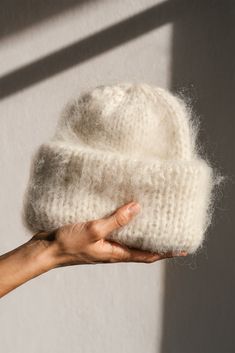 a hand holding a white knitted hat in front of a shadow on the wall