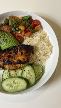 a white plate topped with meat, rice and veggies next to cucumbers