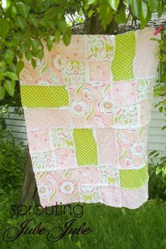 a pink and green patchwork quilt hanging from a tree