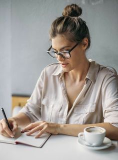 a woman sitting at a table writing on a notepad with a pen in her hand