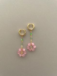 two small pink flowers hanging from gold hoop earrings on a white surface with green beads