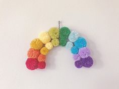 there is a small rainbow decoration hanging on the wall with pom - poms