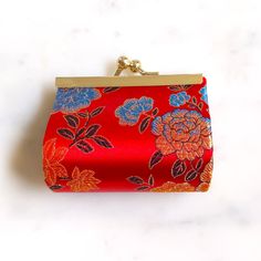 a red purse with blue and orange flowers is on a white surface, next to a gold chain