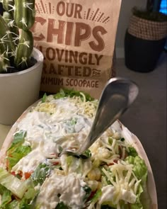 a large salad with cheese and lettuce in a bowl next to a bag of chips