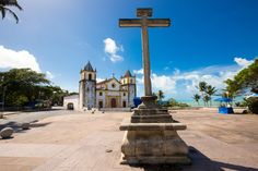 a large cross in front of a church with palm trees and blue sky behind it