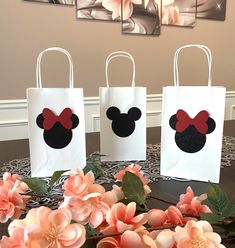 three bags with minnie mouse ears on them are sitting on a table next to flowers