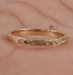 a gold wedding band with leaves on the inside and outside, sitting on a pink background