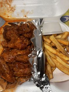 chicken wings and french fries in foil on a plate with a container of dipping sauce