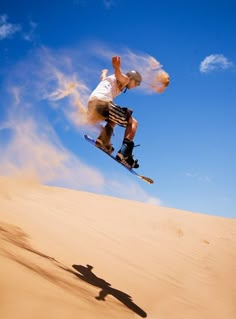 a man flying through the air while riding a snowboard on top of a sandy hill