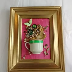 a gold frame with a cup and flowers in it