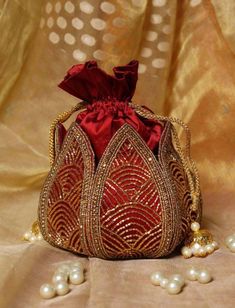 a red bag with pearls on the bottom and gold trimming around it, sitting on a beige cloth