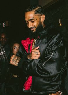 a man in a black jacket and red shirt with tattoos on his arm standing next to other people