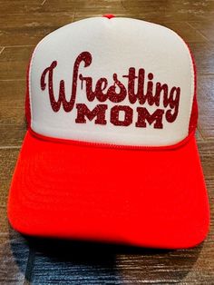 a red and white hat with the words wrestling mom on it sitting on a wooden floor