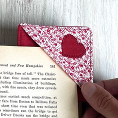 someone is holding an open book with a red heart on it and the pages are folded in half