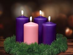 three purple candles sitting next to each other on top of a wooden table covered in greenery