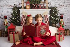 two children sitting on a couch holding christmas books in front of a fireplace with presents around them