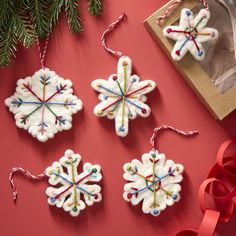 three snowflake ornaments on a red surface next to a christmas tree and ribbon