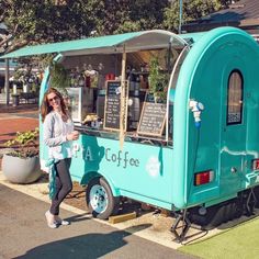 a woman standing in front of a blue coffee cart on the side of a road