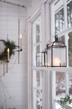 two lanterns hanging from the side of a window with candles in them and greenery