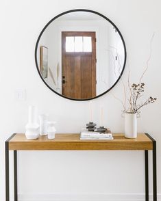 a mirror on the wall above a console table with vases and candles in front of it