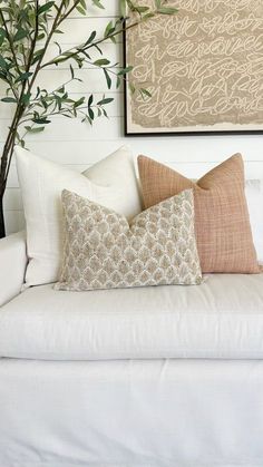 a white couch with two pillows and a plant in the corner on top of it