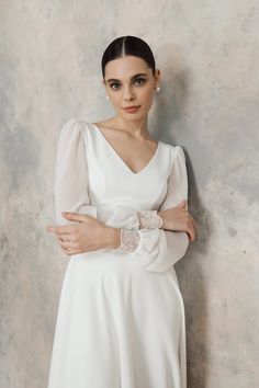 a woman in a white dress leaning against a wall with her hands on her hips