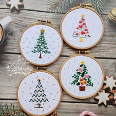 three cross stitch christmas tree ornaments on a wooden table next to cookies and other holiday decorations