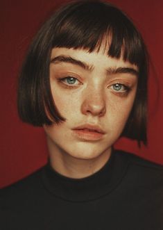 a woman with short hair and blue eyes wearing a black shirt against a red background