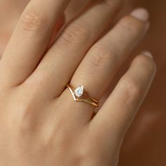 a woman's hand wearing a gold ring with a white diamond on the middle